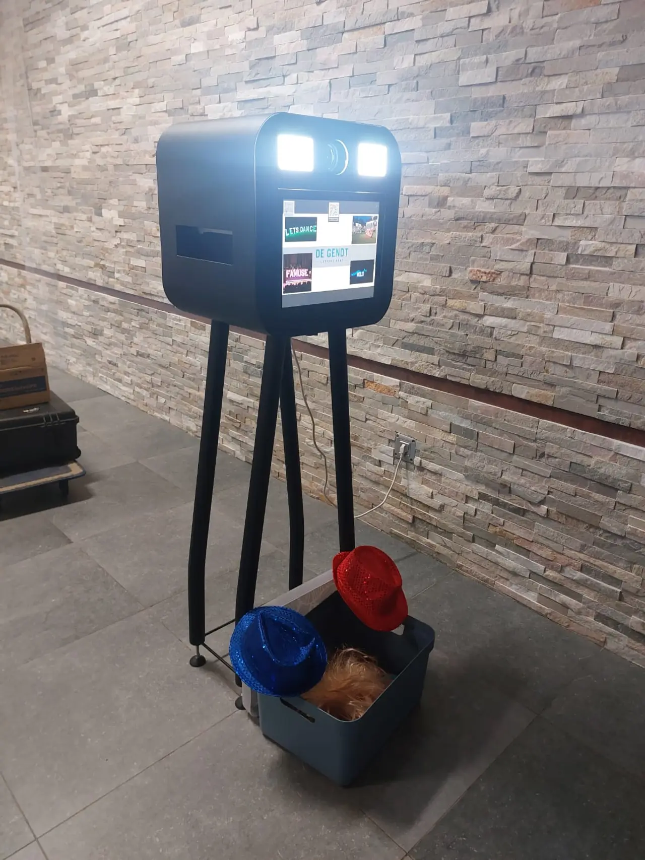 De Cubebooth, een photobooth in kubusvorm op een statief, tegen een stenen muur.