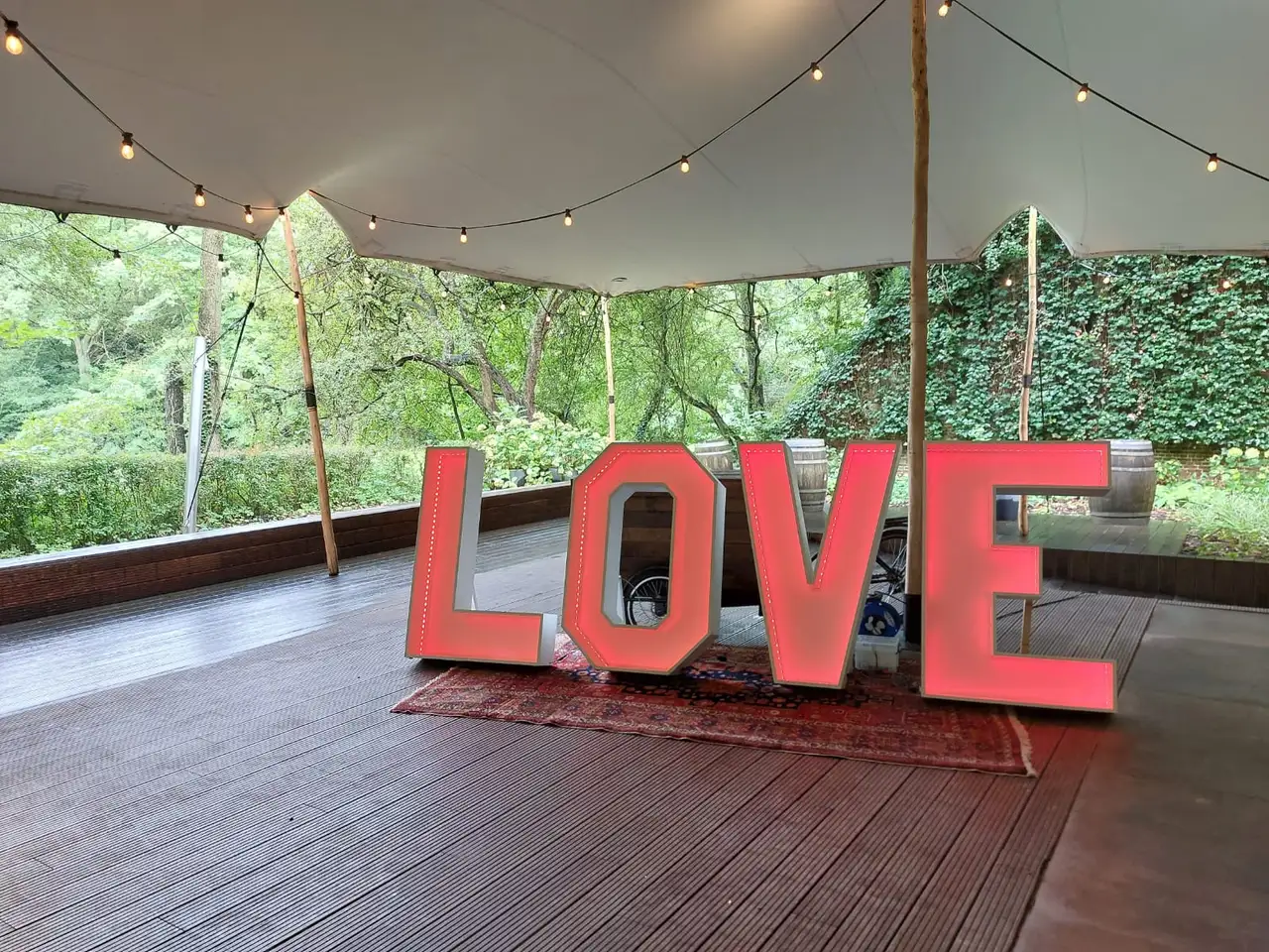 Het woord LOVE in grote letters, verlicht in koraalrood, onder een stretchtent.