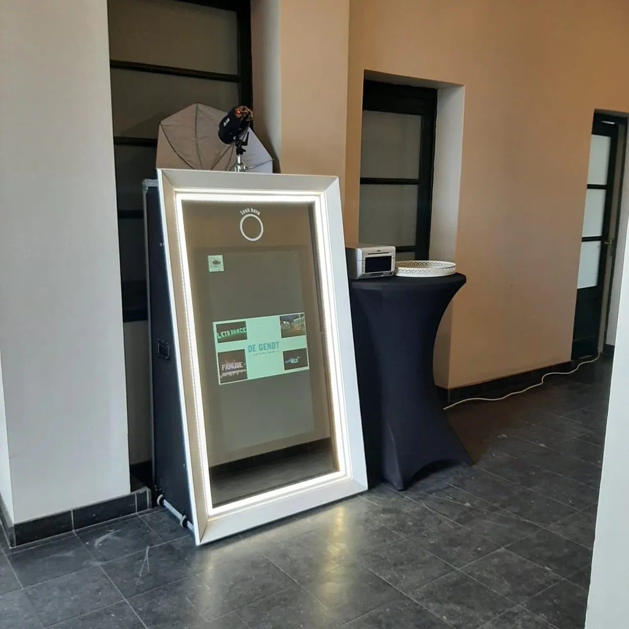 De Mirrorbooth, een manshoge spiegel in een witte lijst met LED-licht, met de fotoprinter op een statafel ernaast.