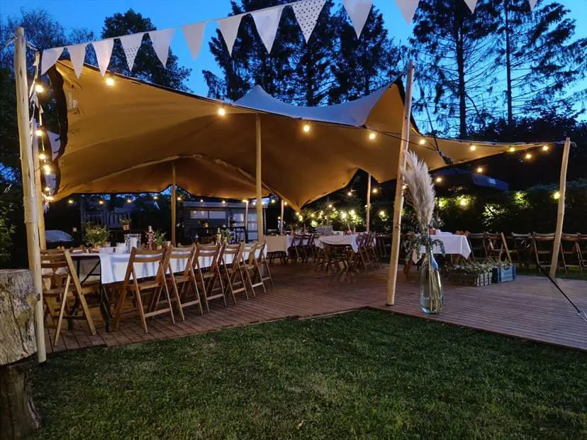 Een stretchtent met lichtslingers boven lange gedekte tafels in een tuin.
