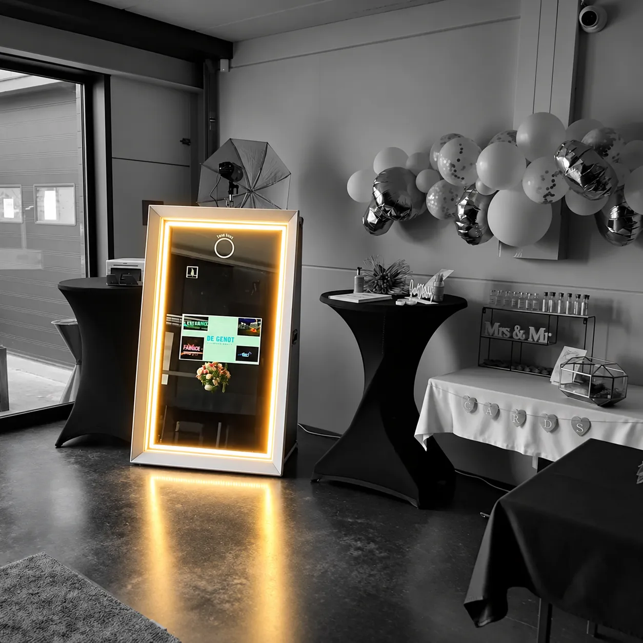 De Mirrorbooth, een spiegel in een witte lijst, tussen twee statafels en een boog van ballonnen.